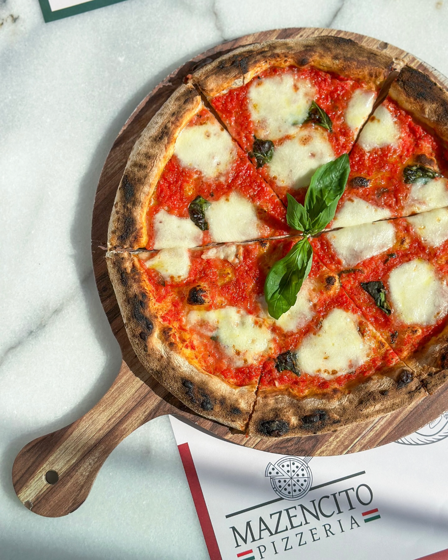 Margherita pizza with basil on a wooden board at Mazencito Pizzeria