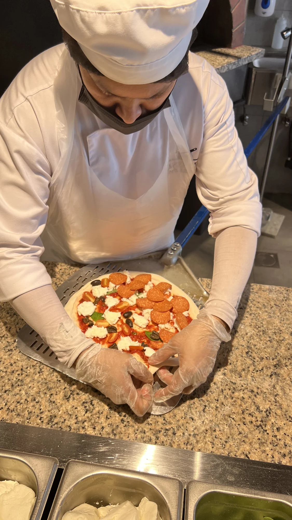 Chef plating a freshly baked pizza at the kitchen pass